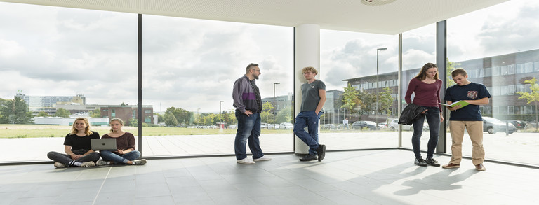 students are talking in front of a large window